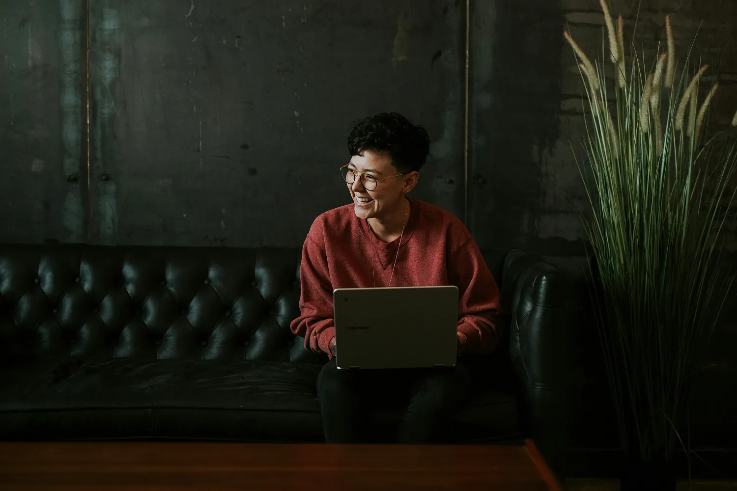 Person smiling with a laptop on a dark couch