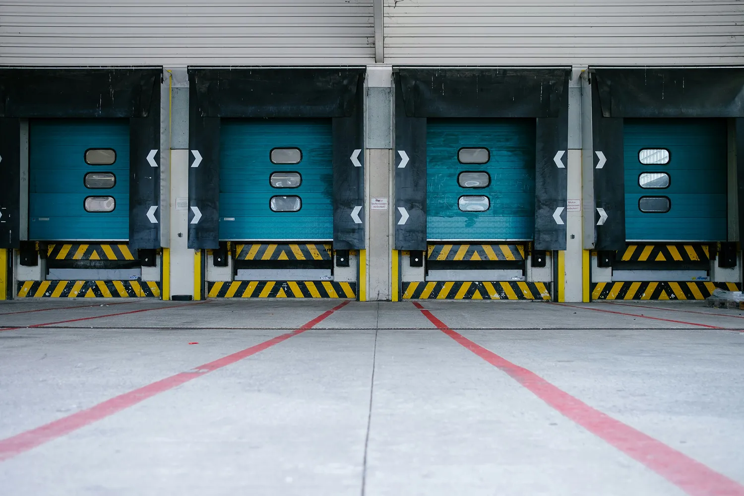 Loading dock with four blue industrial bay doors and black-yellow safety markings