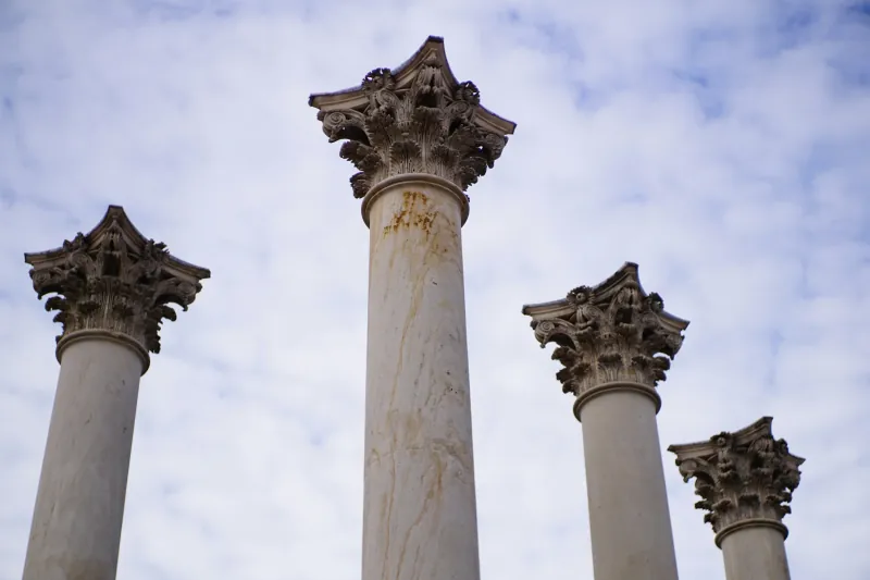 Four ornate stone columns against a cloudy sky