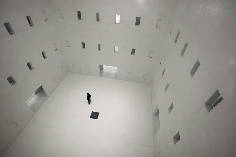 Person standing in a large white atrium with small windows high on the walls
