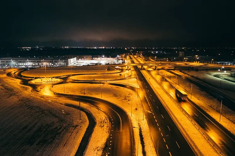 Snowy highway interchange at night with glowing streetlights and light trails from traffic