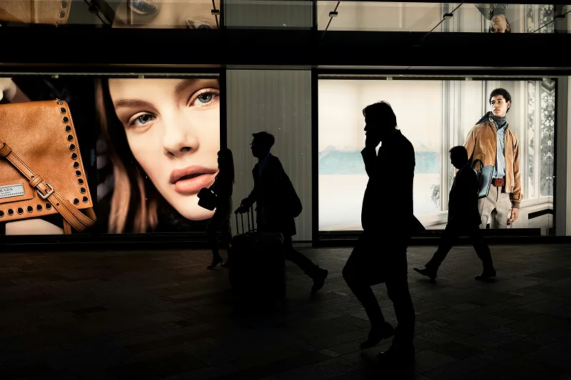Fashion store window display with handbags and models, seen behind silhouetted pedestrians