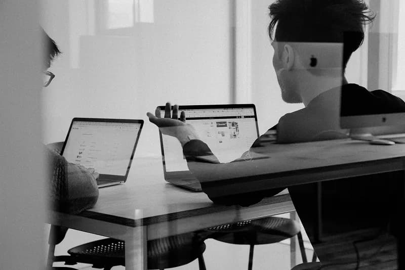 Two people discussing work at a table with laptops open