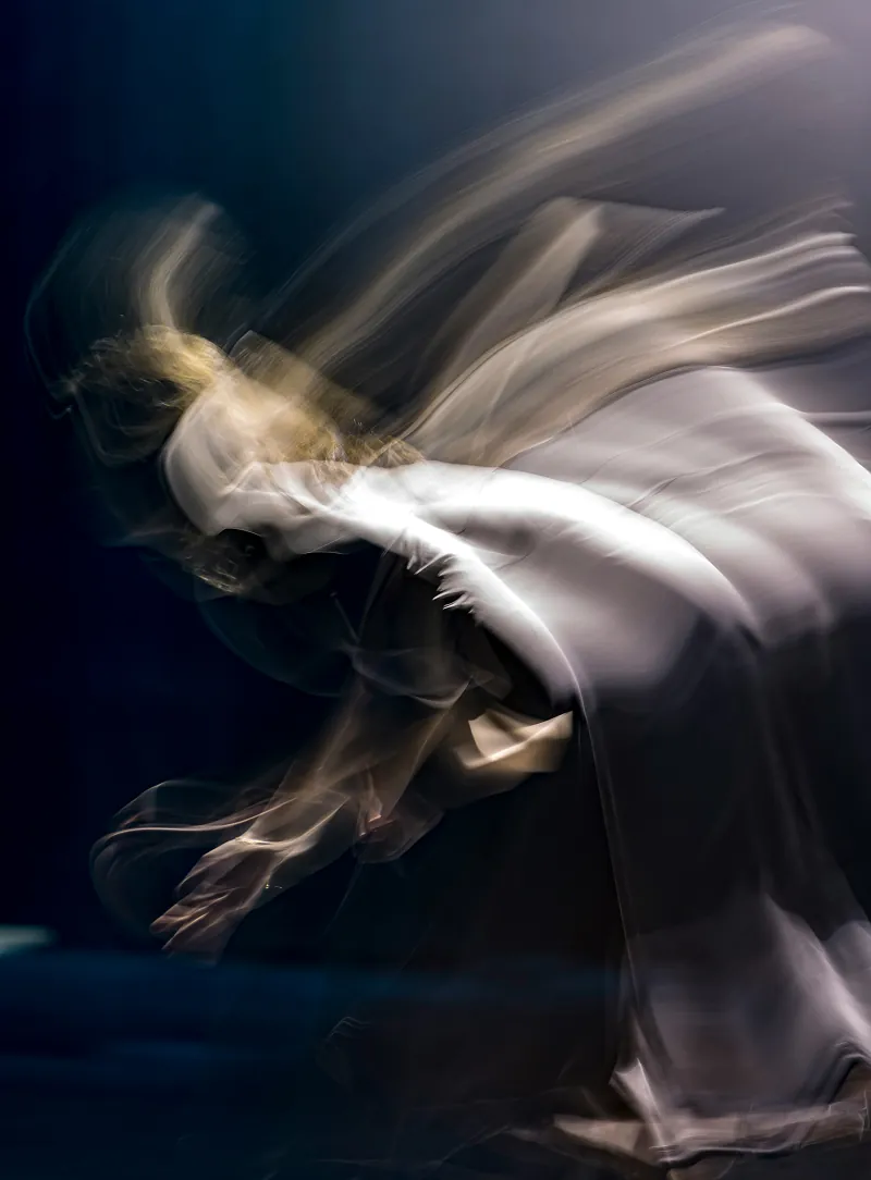 Blurred dancer in flowing white fabric against a dark background