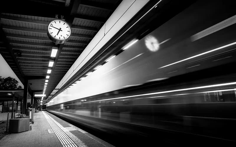 Blurred train passing a station platform with a clock overhead