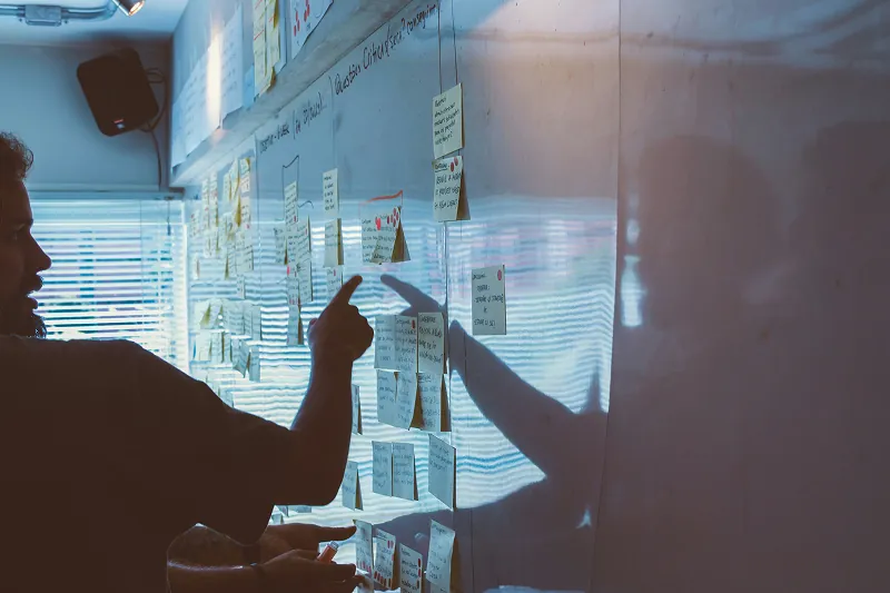 Person pointing at sticky notes on a whiteboard in a meeting room